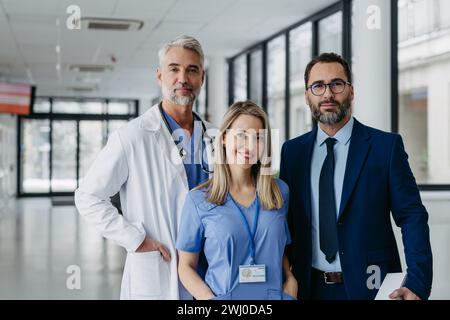 Ritratto di una dottoressa in piedi di fronte a colleghi di sesso maschile. Bella infermiera in uniforme in una moderna clinica privata, che guarda la macchina fotografica. Foto Stock