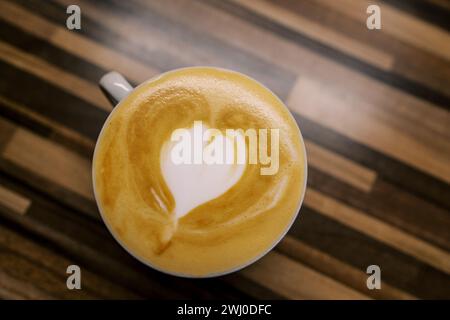 Il cappuccino con il cuore sulla schiuma si trova in una tazza su un tavolo di legno. Vista dall'alto Foto Stock