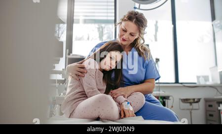 Medico di supporto lenire un paziente di bambini preoccupati in pronto soccorso. Abbracciare la bambina prima dell'intervento. Abbracciare la bambina prima dell'intervento Foto Stock