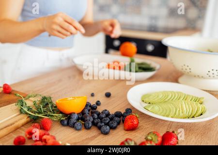 Una giovane ragazza sta preparando una colazione vegana in cucina. Primo piano di un piatto con avocado, rucola, frutti di bosco e agrumi Foto Stock