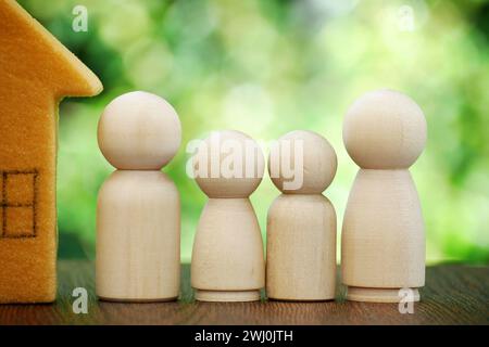Casa famiglia in miniatura e bambole di legno. Concetto di protezione e sicurezza, sicurezza domestica, assicurazione di proprietà, casa, famiglia felice, sponsorizzazione di minori, m Foto Stock