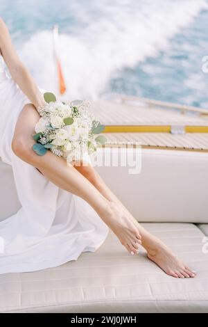 La sposa con un bouquet si siede a bordo di uno yacht che naviga sul mare. Ritagliato. Senza volto Foto Stock