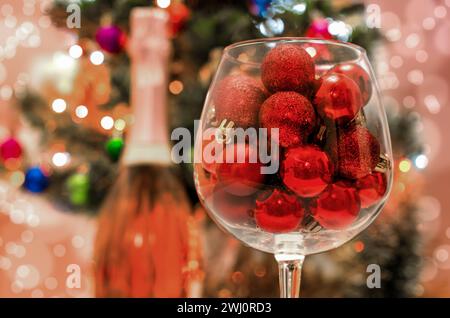 Palline rosse glitterate in un grande bicchiere di vino da vicino sullo sfondo di un albero di Natale decorato Foto Stock