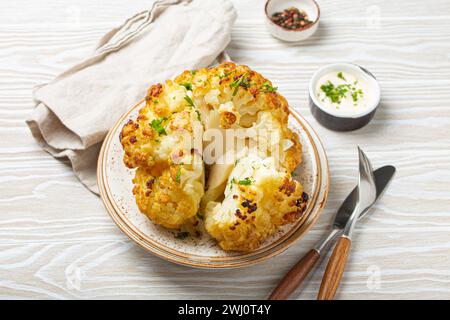 Testa di cavolfiore arrosto intera con olio d'oliva su piatto su tavola rustica in legno bianco vista dall'alto con posate. Piatto vegetariano. Foto Stock