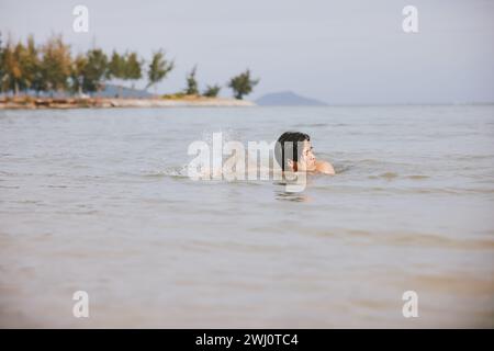 Uomo asiatico attivo che si gode una nuotata tropicale nelle rinfrescanti acque dell'Oceano Blu durante una vacanza rilassante Foto Stock