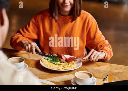 donna felice che fa colazione vicino alla sua tazza di caffè mentre si gode un pasto gustoso vicino al ragazzo nero Foto Stock