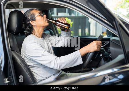 Un giovane asiatico ubriaco guida un'auto con una bottiglia di birra, un concetto di guida pericoloso. Foto Stock