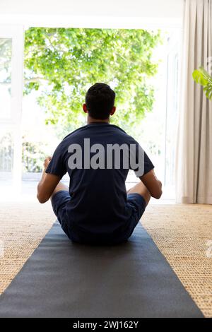 Uomo birazziale che fa yoga e meditando a casa Foto Stock