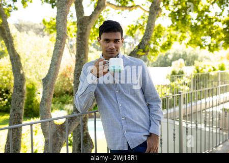 Ritratto di un felice uomo birazziale che tiene la tazza sul balcone a casa Foto Stock