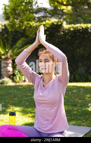 Felice donna birazziale che pratica meditazione yoga seduto in un giardino soleggiato Foto Stock