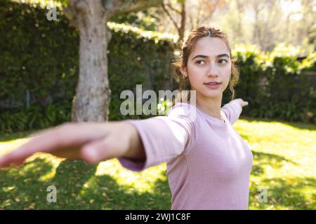 Felice donna birazziale che pratica yoga in piedi e si allunga in un giardino soleggiato Foto Stock