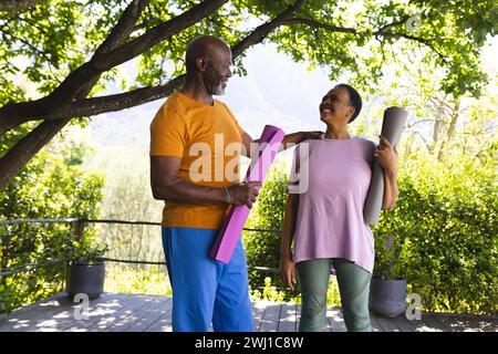 Amici anziani felici e diversificati, uomini e donne, che parlano alla lezione di yoga nel giardino soleggiato Foto Stock