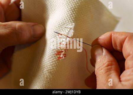 donna che cucisce un panno bianco strappato con filo rosso Foto Stock