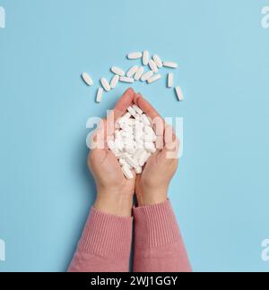 Due mani femminili trattengono pillole ovali bianche su sfondo blu, vista dall'alto Foto Stock