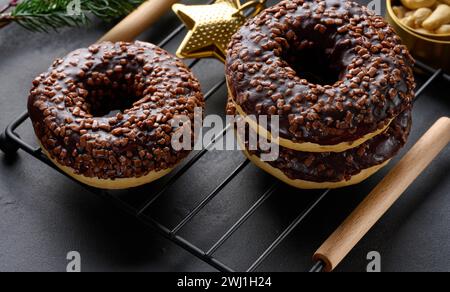 Ciambelle al cioccolato cosparse di noci schiacciate su un tavolo nero Foto Stock