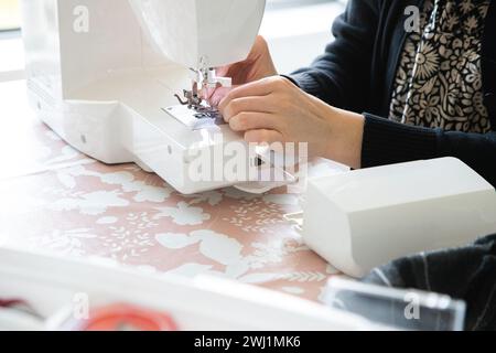 Mano di donna davanti alla macchina da cucire per infilare l'ago e poi cucire. Precisione e dettagli minimi. Foto Stock