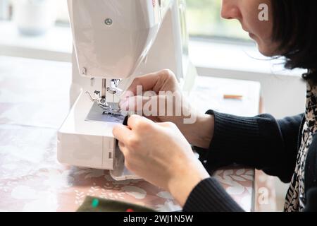 Mano di donna davanti alla macchina da cucire per infilare l'ago e poi cucire. Precisione e dettagli minimi. Foto Stock