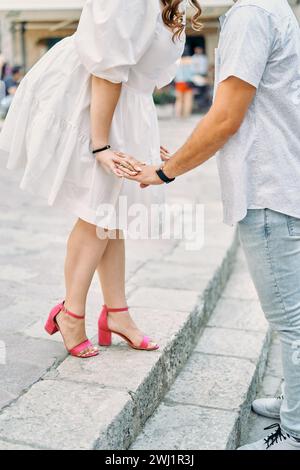 La donna si inclinava verso un uomo che le teneva le mani mentre si trovava sui gradini. Ritagliato. Senza volto Foto Stock