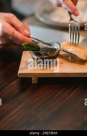 Primo piano delle mani di un uomo che tiene un coltello e una forchetta, che raccoglie un pezzo di cibo impanato su un tavolo di legno. Foto Stock