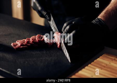 Primo piano di uno chef che indossa guanti neri che affetta sapientemente carne, mostrando precisione culinaria e igiene Foto Stock