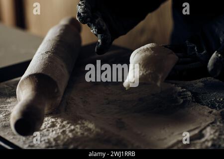 Indossa guanti neri che modellano delicatamente l'impasto, mostrando meticolosa abilità culinaria e cura nella preparazione degli alimenti Foto Stock