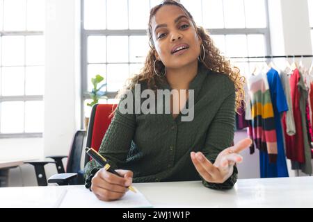 Felice stilista birazziale che partecipa a una videochiamata e prende appunti alla scrivania in studio. Moda, design, creatività, abbigliamento e piccole imprese, Foto Stock