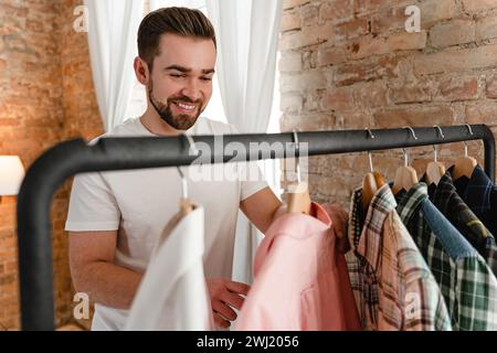 L'uomo sta sfogliando le sue varie camicie appese al portabiti nel guardaroba Foto Stock