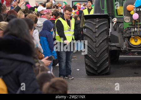 Coblenza, Germania. 12 febbraio 2024. I dipendenti di un servizio di sicurezza proteggono le ruote dei trattori durante la sfilata del lunedì delle rose di Coblenza. 155 numeri sfilano per tutta la città. Crediti: Thomas Frey/dpa/Alamy Live News Foto Stock