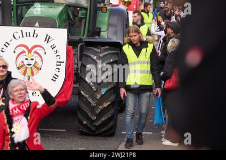 Coblenza, Germania. 12 febbraio 2024. I dipendenti di un servizio di sicurezza proteggono le ruote dei trattori durante la sfilata del lunedì delle rose di Coblenza. 155 numeri sfilano per tutta la città. Crediti: Thomas Frey/dpa/Alamy Live News Foto Stock