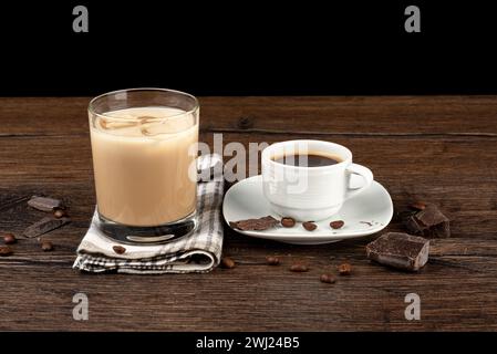 Chicchi di caffè con pezzi di cioccolato, una tazza di caffè e un bicchiere di liquore irlandese in un bicchiere con ghiaccio. Sfondo in legno, spazio per copiare. Foto Stock