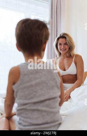 La madre felice e il figlio piccolo si impegnano in un gioco allegro, creando ricordi preziosi mentre si legano nel comfort del loro letto Foto Stock