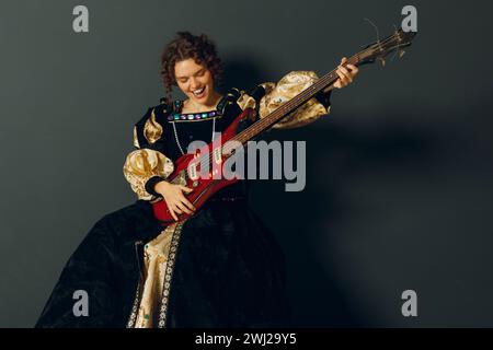 Ritratto di una giovane donna adulta che suona musica con la chitarra elettrica e indossa un abito medievale. Foto Stock