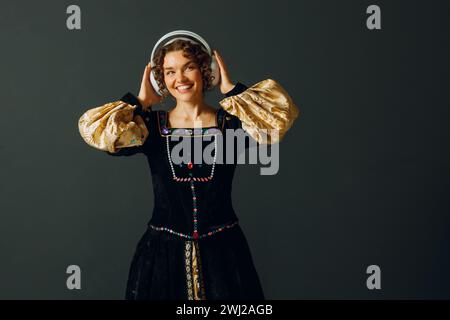 Ritratto di una giovane donna rinascimentale con le cuffie e la testa toccante e vestito con un abito medievale ascolta musica. Foto Stock