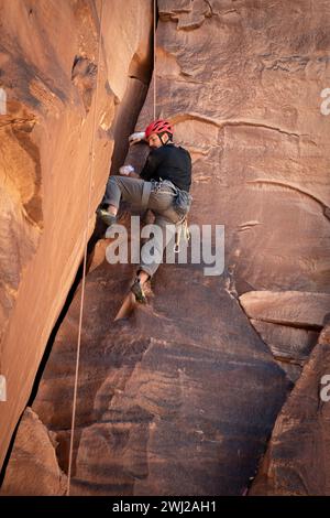 Vista ad angolo basso dell'uomo determinato che sale dalla scogliera rocciosa Foto Stock