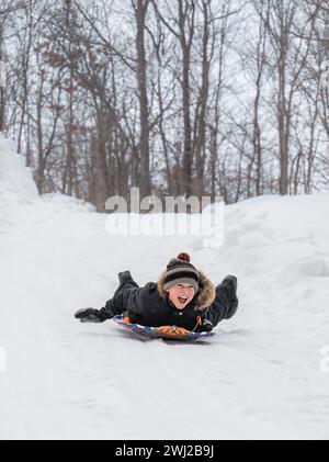 Allegro ragazzo che scende in slitta da una collina innevata in una fredda giornata invernale. Foto Stock