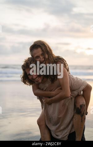 Uomo Donna piggybacking passeggiando sul lungomare a beach Foto Stock