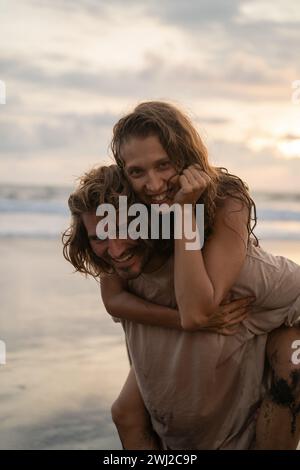 Uomo Donna piggybacking passeggiando sul lungomare a beach Foto Stock