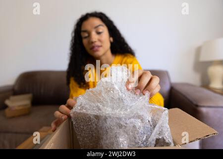 Donna birazziale con maglione giallo che apre il pacco a casa Foto Stock