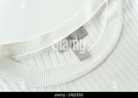 Primo piano di uno scollo in maglia bianca con un'etichetta grigia che mette in risalto la texture e la qualità del tessuto Foto Stock