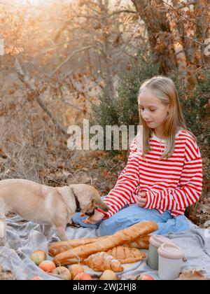 La giovane ragazza seduto su un plaid dà da mangiare al cane durante un picnic Foto Stock