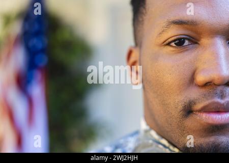 Un soldato afroamericano focalizzato affronta da vicino fuori casa con la bandiera degli stati uniti e lo spazio per le copie Foto Stock