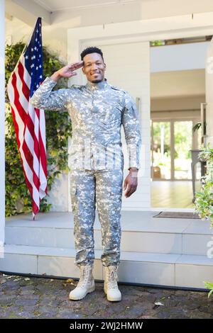 Felice soldato afroamericano in piedi e salutando fuori casa con la bandiera degli stati uniti, spazio copia Foto Stock
