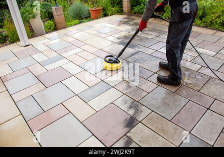 Pulizia delle lastre di pietra sul patio con il pulitore ad alta pressione. Persona operante che pulisce l'esterno Foto Stock