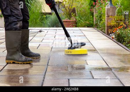 Pulizia delle lastre di pietra sul patio con il pulitore ad alta pressione. Persona operante che pulisce l'esterno Foto Stock