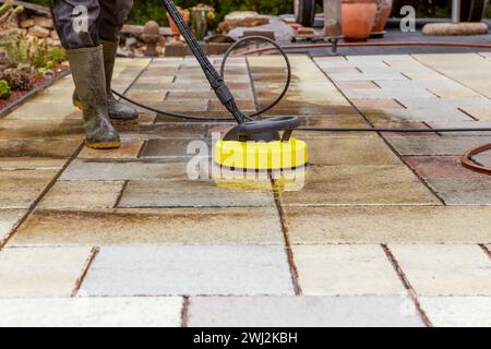 Pulizia delle lastre di pietra sul patio con il pulitore ad alta pressione. Persona operante che pulisce l'esterno Foto Stock