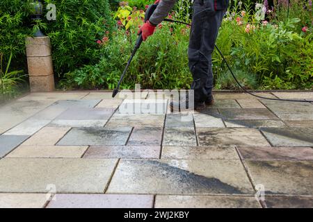 Pulizia delle lastre di pietra sul patio con il pulitore ad alta pressione. Persona operante che pulisce l'esterno Foto Stock