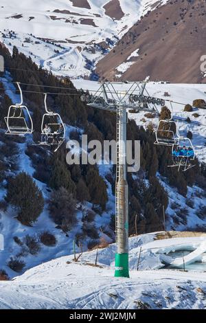 Le persone siedono sulle sedie della funivia che porta alla cima della pista da sci. Palo della funivia, costruzione. Attività per le vacanze invernali, sciatori, snowboarder, festa Foto Stock