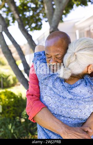 Una coppia di anziani felice e variegata abbracciata in un giardino soleggiato Foto Stock