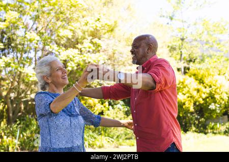 Coppia di anziani felice e variegata che balla nel giardino soleggiato Foto Stock