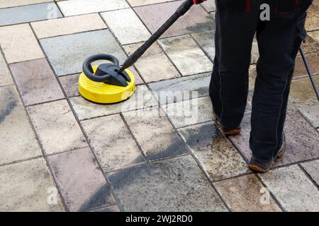 Pulizia delle lastre di pietra sul patio con il pulitore ad alta pressione. Persona operante che pulisce l'esterno Foto Stock